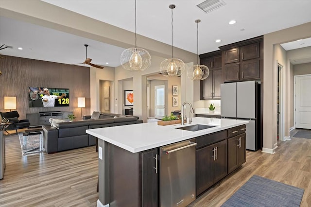 kitchen with sink, dishwasher, a kitchen island with sink, fridge, and decorative light fixtures