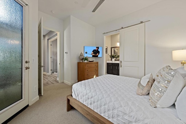 carpeted bedroom featuring ensuite bathroom, a barn door, and ceiling fan