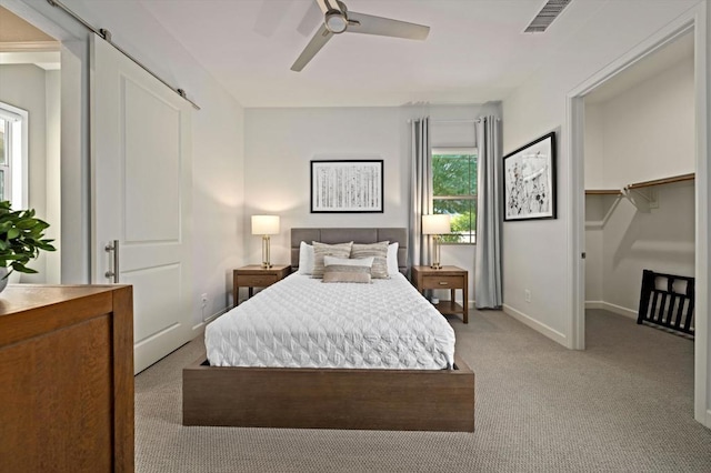 carpeted bedroom featuring a walk in closet, a barn door, and ceiling fan