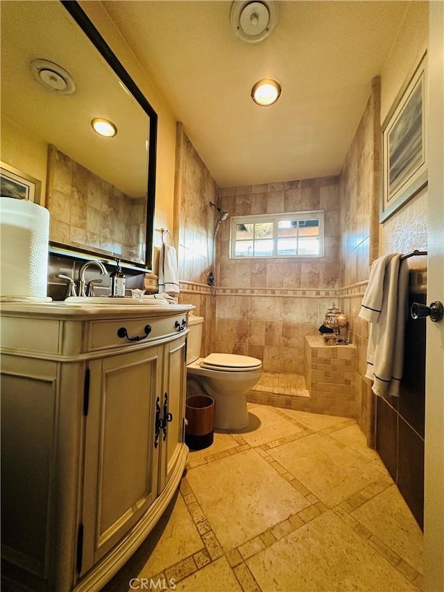 bathroom featuring tiled shower, vanity, toilet, and tile walls