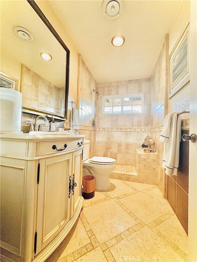 bathroom featuring tiled shower, vanity, toilet, and tile walls