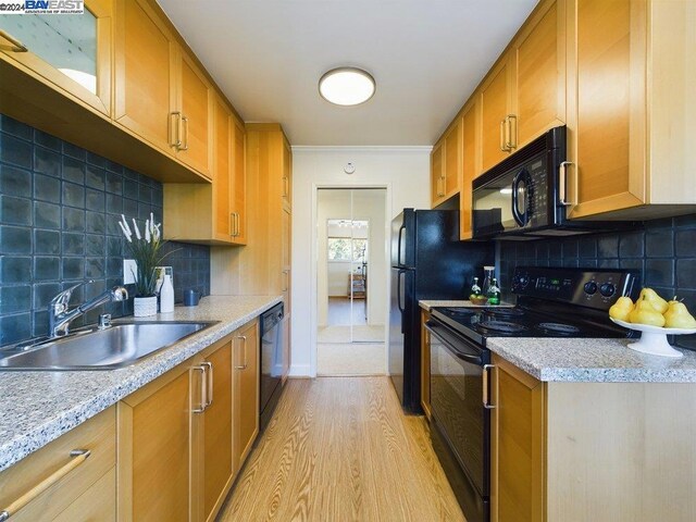 kitchen with light hardwood / wood-style floors, tasteful backsplash, light stone countertops, black appliances, and sink