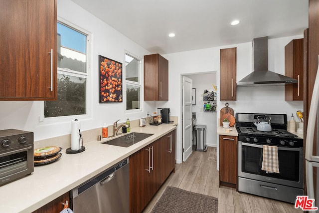 kitchen featuring sink, stainless steel appliances, wall chimney range hood, and light wood-type flooring