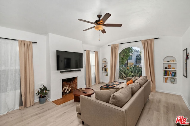 living room with built in shelves, vaulted ceiling, ceiling fan, and light hardwood / wood-style flooring