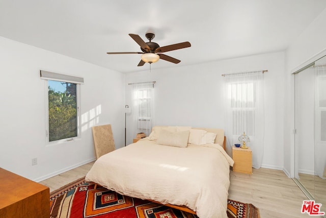 bedroom featuring ceiling fan, light hardwood / wood-style floors, a closet, and multiple windows