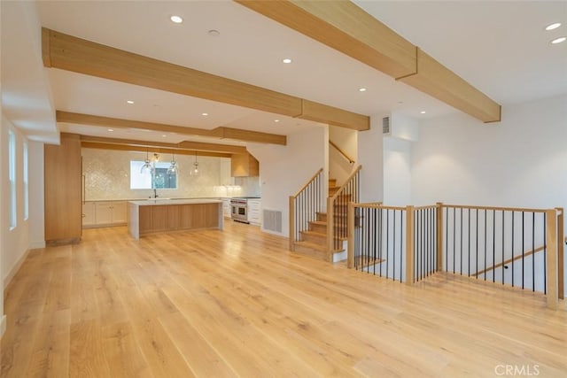 unfurnished living room with beam ceiling, light hardwood / wood-style flooring, and sink