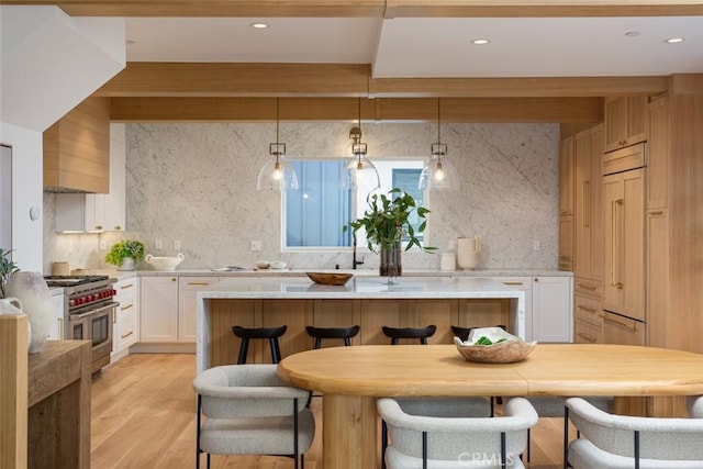 kitchen with pendant lighting, a breakfast bar, white cabinets, light wood-type flooring, and premium appliances