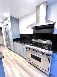 kitchen featuring wall chimney range hood, blue cabinetry, stainless steel range, and light hardwood / wood-style flooring