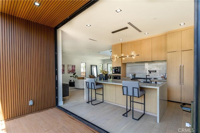 kitchen featuring tasteful backsplash, pendant lighting, light hardwood / wood-style floors, a kitchen island with sink, and a breakfast bar