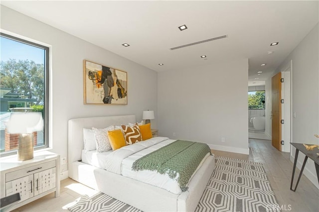 bedroom with light wood-type flooring, connected bathroom, and multiple windows