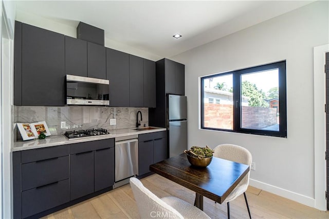 kitchen featuring appliances with stainless steel finishes, light wood-type flooring, backsplash, and sink