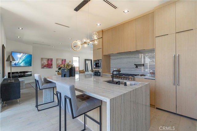 kitchen featuring light brown cabinets, stainless steel oven, light hardwood / wood-style flooring, a breakfast bar area, and a kitchen island with sink