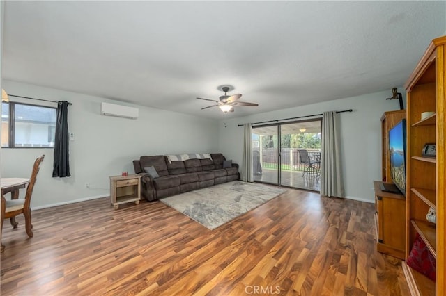 living room with a ceiling fan, an AC wall unit, baseboards, and wood finished floors