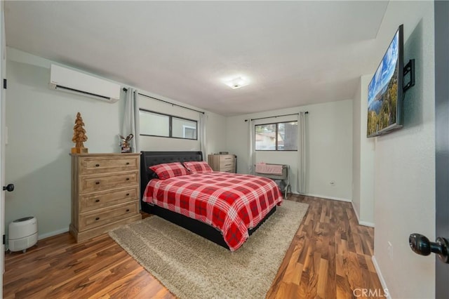 bedroom with a wall unit AC, baseboards, and wood finished floors