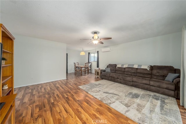 living room with a wall mounted air conditioner, ceiling fan, baseboards, and wood finished floors