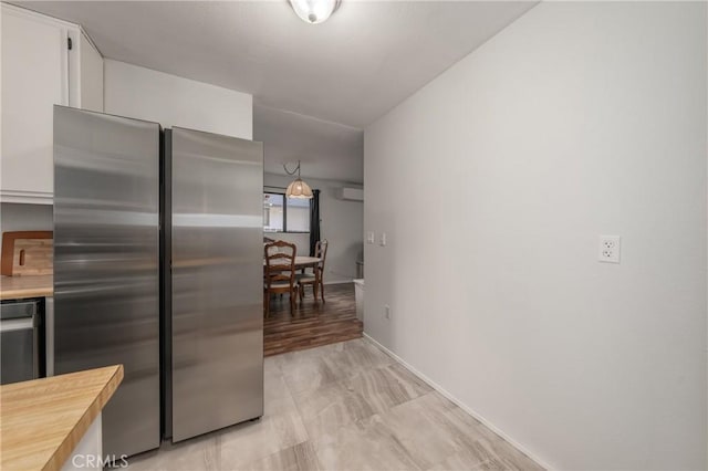 kitchen with butcher block countertops, freestanding refrigerator, white cabinets, and baseboards