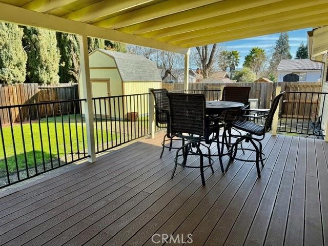 deck with an outbuilding, a fenced backyard, a yard, a shed, and outdoor dining space