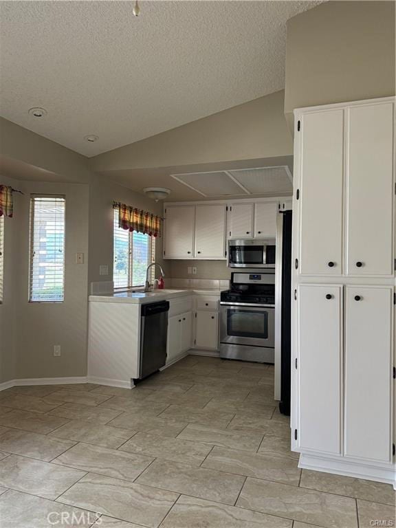 kitchen with a textured ceiling, vaulted ceiling, stainless steel appliances, and white cabinetry