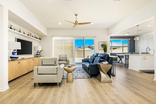 living room featuring ceiling fan, sink, and light wood-type flooring