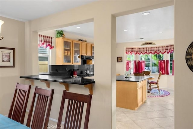 kitchen with a kitchen breakfast bar, kitchen peninsula, decorative backsplash, light brown cabinetry, and light tile patterned floors