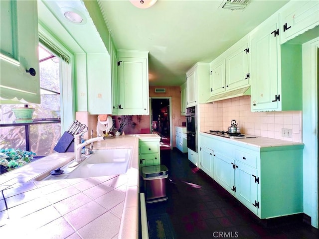 kitchen featuring tasteful backsplash, white cabinets, under cabinet range hood, gas stovetop, and a sink