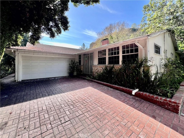 ranch-style house with an attached garage, a chimney, decorative driveway, and stucco siding