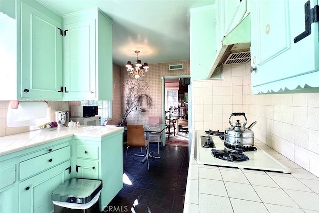 kitchen featuring a notable chandelier, tile counters, tasteful backsplash, white gas stovetop, and hanging light fixtures