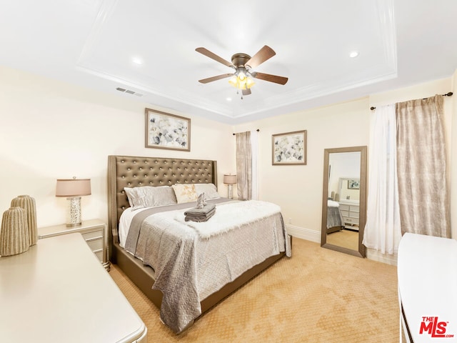 bedroom with a raised ceiling, light colored carpet, and ceiling fan