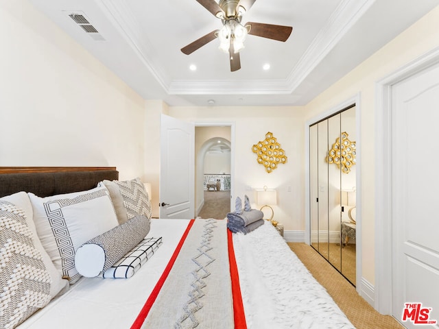 carpeted bedroom with ceiling fan, crown molding, a tray ceiling, and a closet