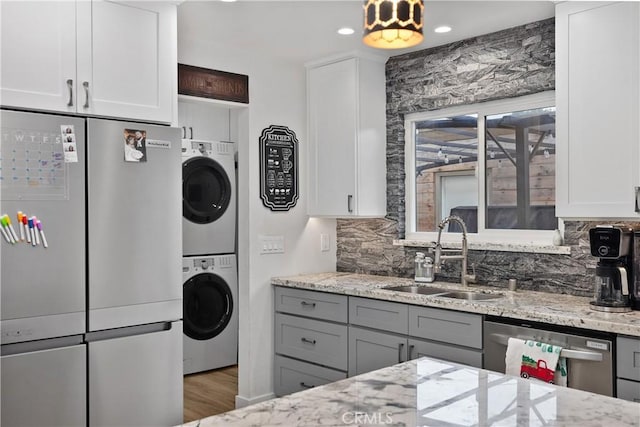 kitchen featuring light stone countertops, white cabinetry, sink, stacked washer and dryer, and appliances with stainless steel finishes