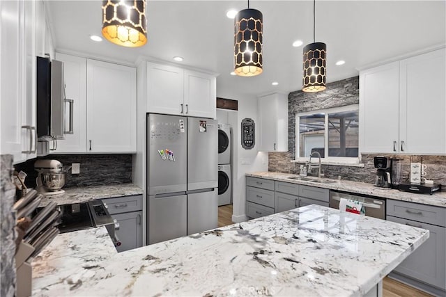 kitchen featuring light stone countertops, white cabinetry, sink, stainless steel appliances, and stacked washer and clothes dryer