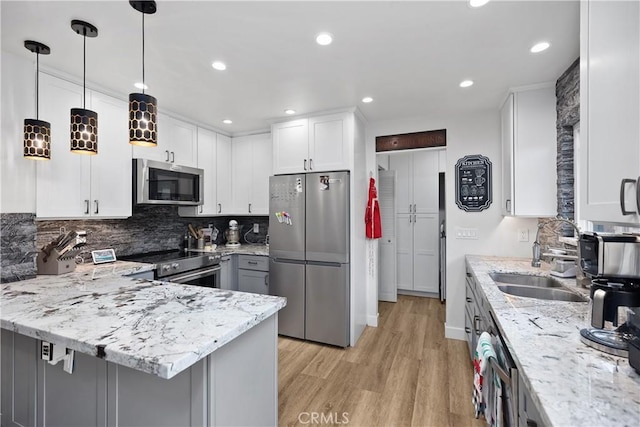 kitchen featuring light stone counters, stainless steel appliances, decorative light fixtures, white cabinets, and light hardwood / wood-style floors