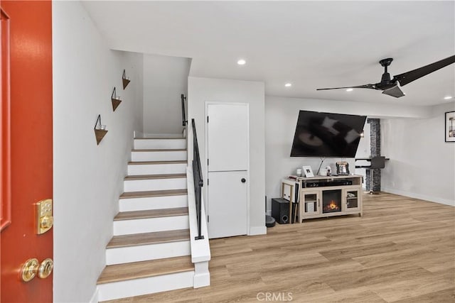 staircase featuring ceiling fan, a fireplace, and wood-type flooring