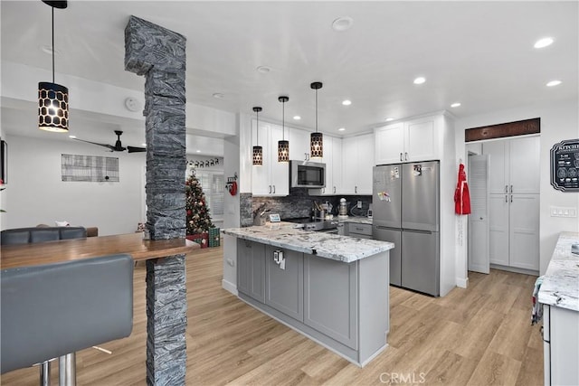 kitchen featuring light stone countertops, stainless steel appliances, decorative light fixtures, white cabinets, and light wood-type flooring