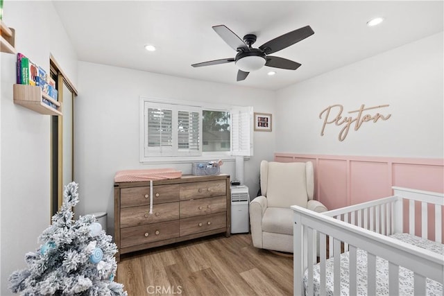 bedroom with ceiling fan, a nursery area, and light wood-type flooring