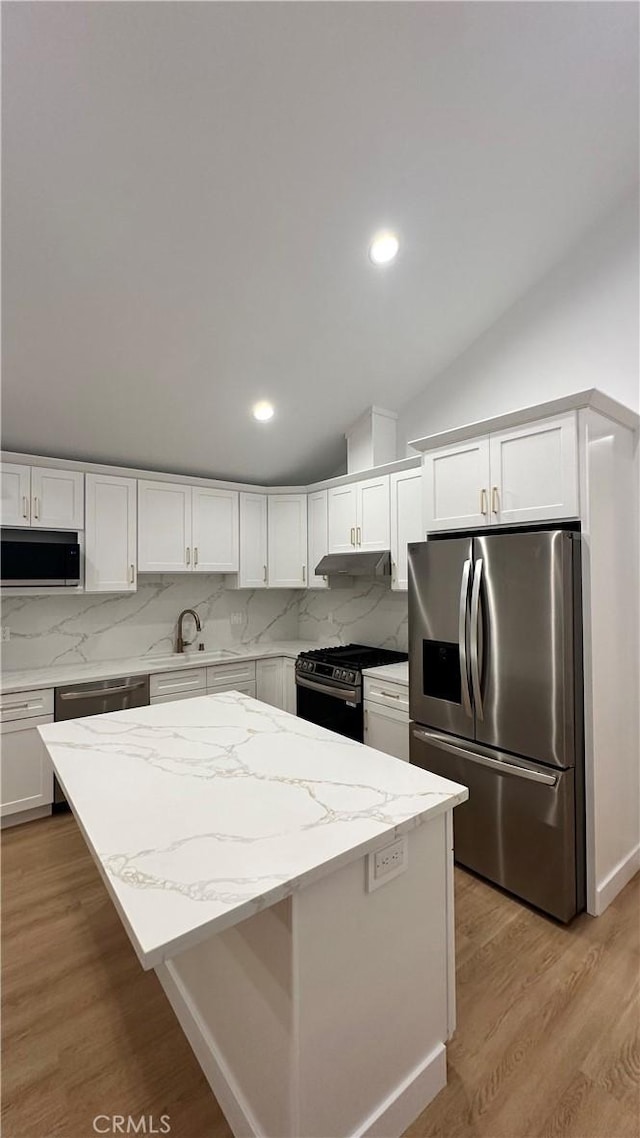 kitchen with light wood finished floors, appliances with stainless steel finishes, a center island, a sink, and backsplash