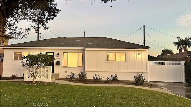 view of front of home with roof with shingles, a front yard, and fence