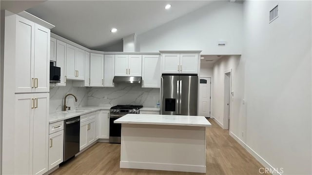 kitchen with a kitchen island, appliances with stainless steel finishes, light wood-type flooring, under cabinet range hood, and a sink