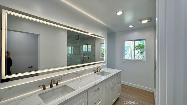 bathroom with a marble finish shower, baseboards, a sink, and wood finished floors