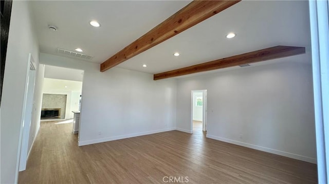 spare room with a large fireplace, beamed ceiling, wood finished floors, and visible vents