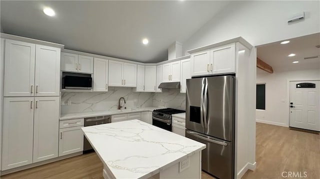 kitchen with light wood finished floors, stainless steel appliances, lofted ceiling, backsplash, and a sink