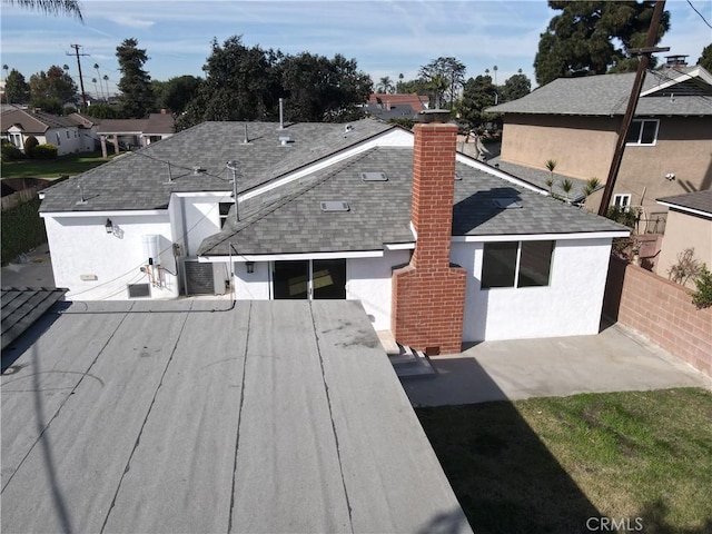 exterior space featuring a shingled roof, a residential view, fence, central air condition unit, and stucco siding