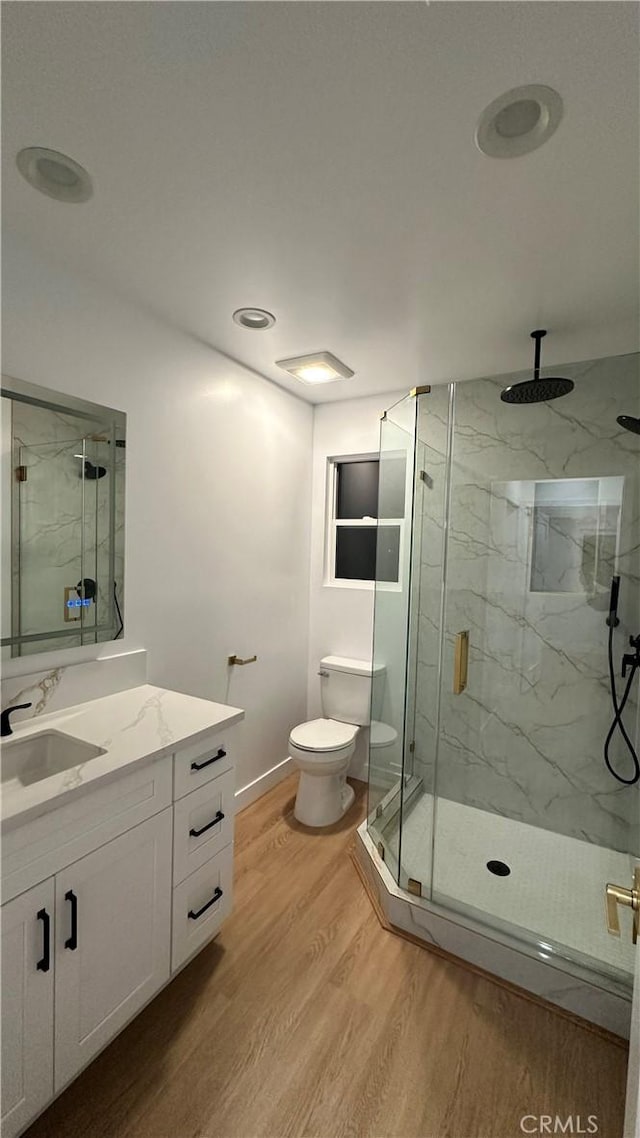 bathroom featuring toilet, wood finished floors, vanity, baseboards, and a marble finish shower