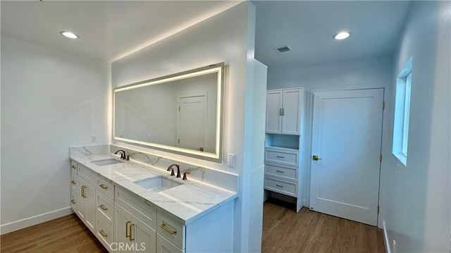 bathroom featuring double vanity, wood finished floors, a sink, and visible vents