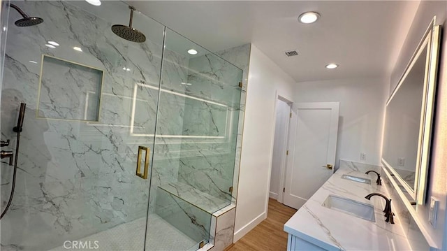 bathroom featuring double vanity, a sink, a marble finish shower, and wood finished floors