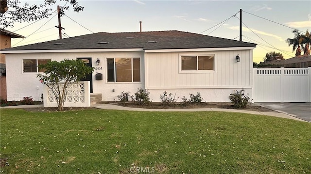 view of front facade featuring roof with shingles, fence, and a front yard