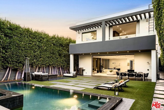 back house at dusk with a patio, outdoor lounge area, a lawn, and a balcony