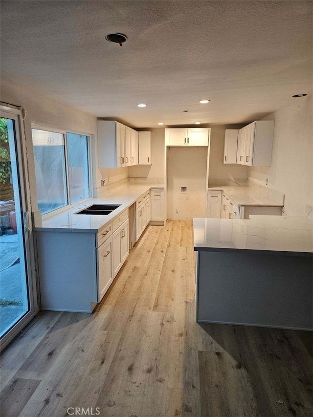 kitchen with white cabinets, a textured ceiling, light wood-type flooring, and sink