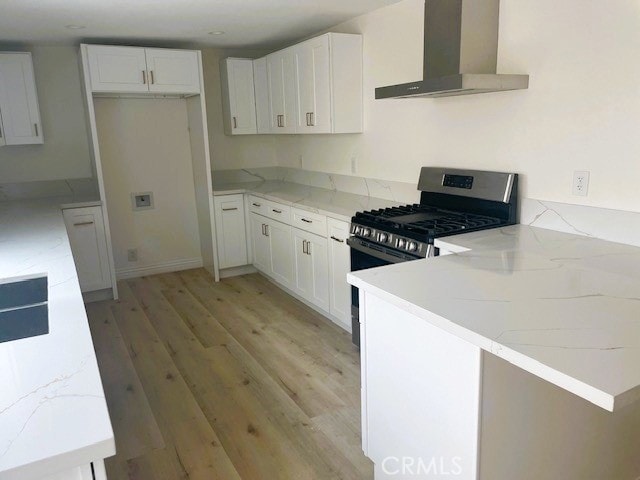 kitchen with light stone countertops, a peninsula, stainless steel gas range oven, wall chimney exhaust hood, and light wood-type flooring