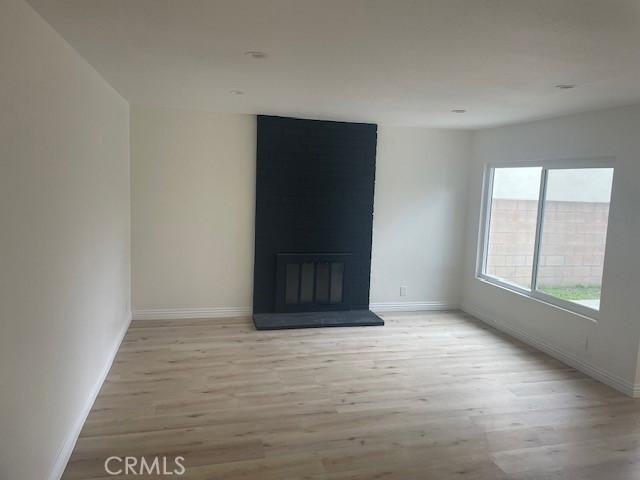 spare room with a large fireplace, light wood-style flooring, and baseboards